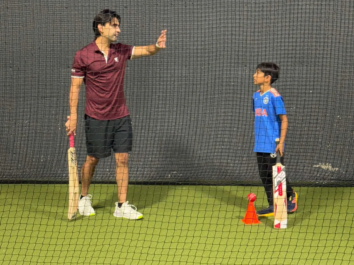 A coach talking a young batter through a drill in the nets